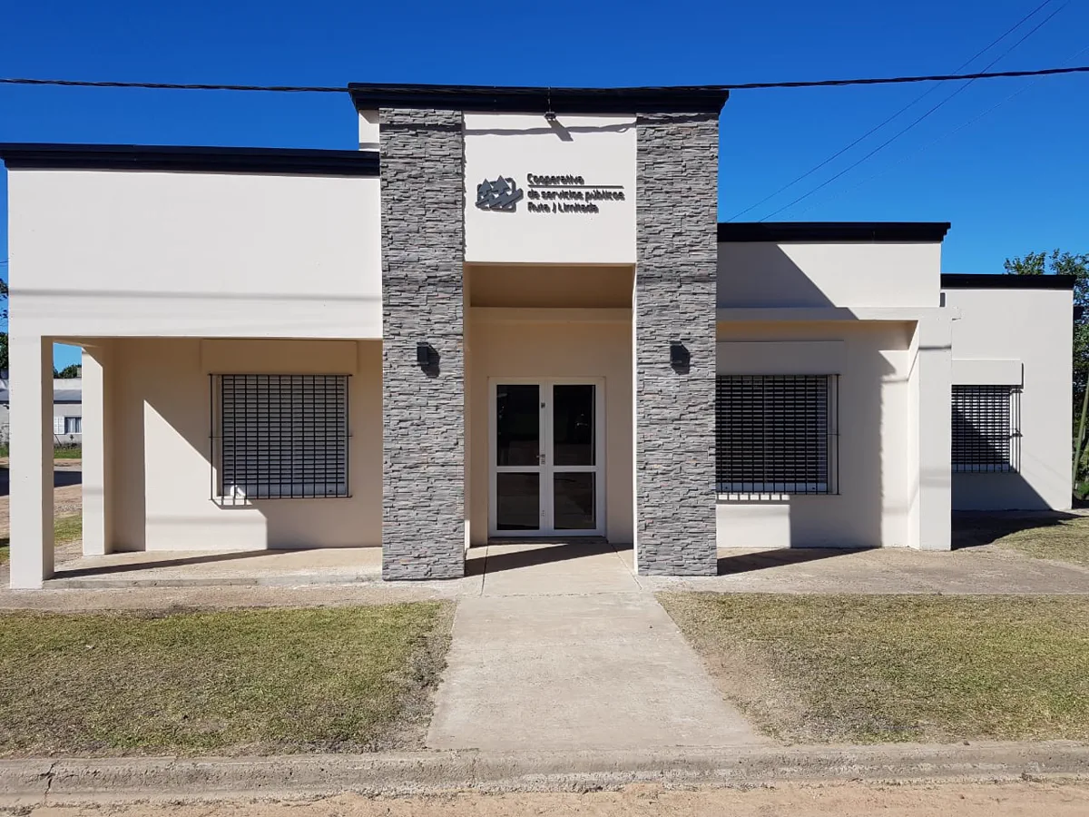 Frente actual de las oficinas de la Cooperativa Ruta J: fachada blanca con columnas de piedra y el cartel &ldquo;Cooperativa de servicios públicos Ruta J Limitada&rdquo; sobre la entrada