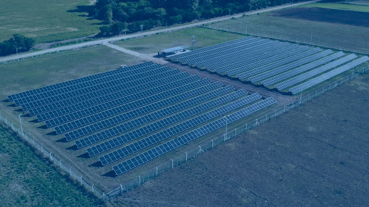 Vista aérea del Parque Solar Ruta J: dos conjuntos de hileras de paneles fotovoltaicos en un predio rural cercado